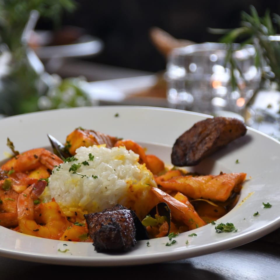 White plate of seasoned rice, sautéed shrimp, roasted vegetables, and grilled meat garnished with parsley.