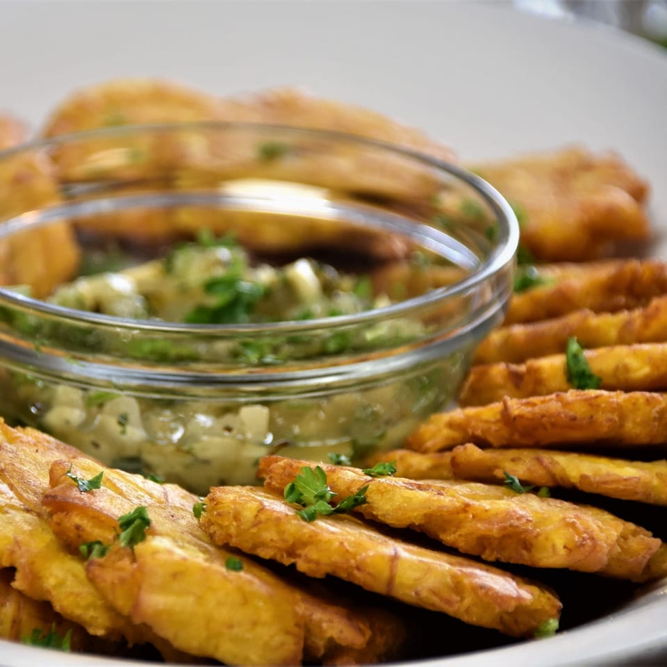Golden fried appetizers garnished with parsley surround a glass bowl of creamy herb dipping sauce.