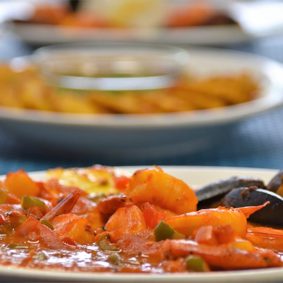Close-up of shrimp and mussels in a tomato-based sauce with chopped green herbs on a plate.