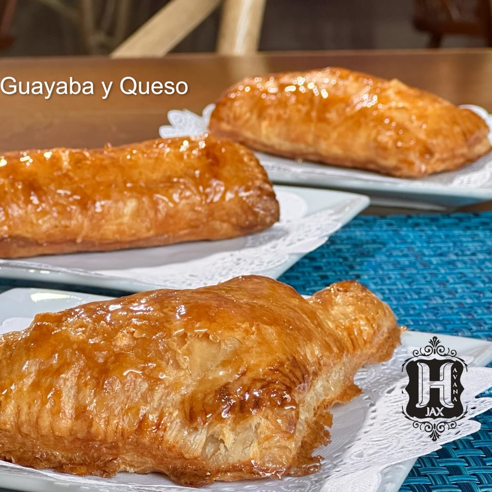 Glazed golden pastries filled with guava and cheese, arranged on decorative plates.
