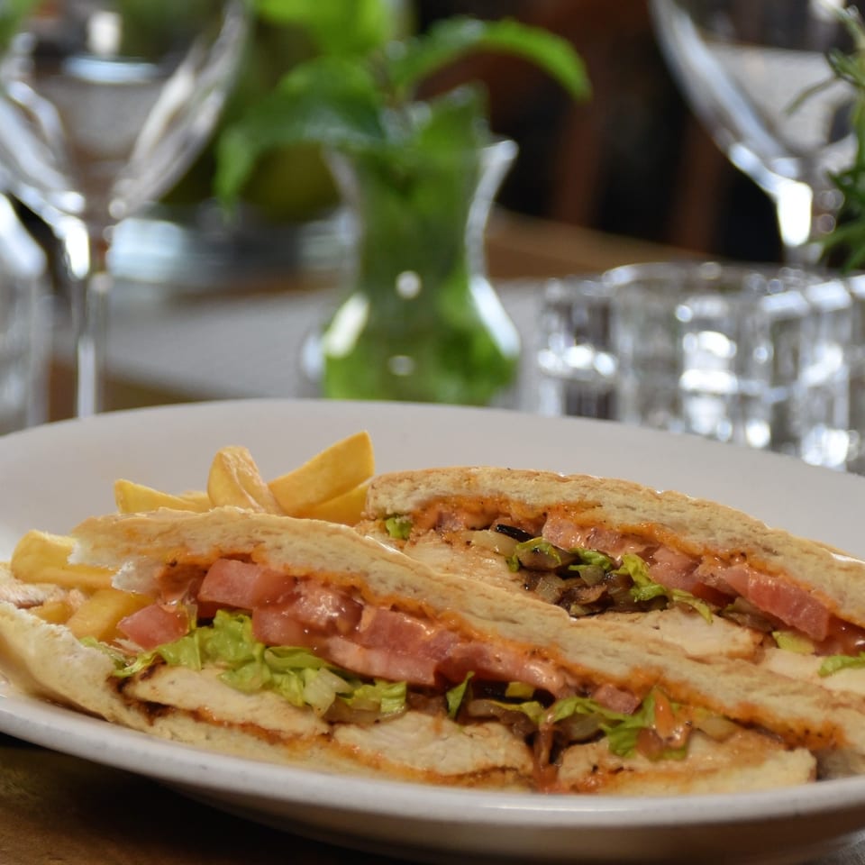 Two stuffed flatbread sandwiches with lettuce, tomatoes, mushrooms, sauce, and potato wedges on a plate.