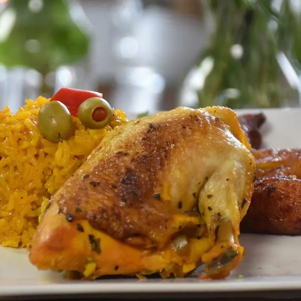 Cuban-style roasted chicken with yellow rice, garnished with green olives and red pepper.