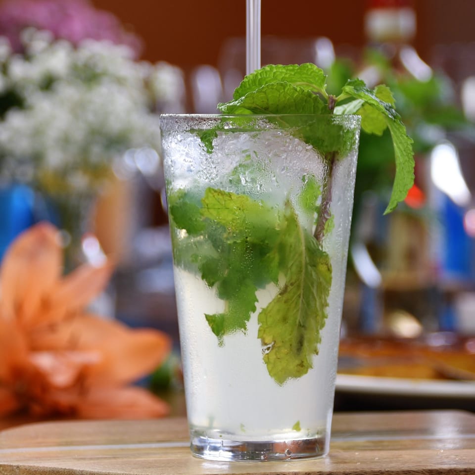 Mojito with mint leaves, lime, ice, and condensation in a tall glass on a restaurant table.