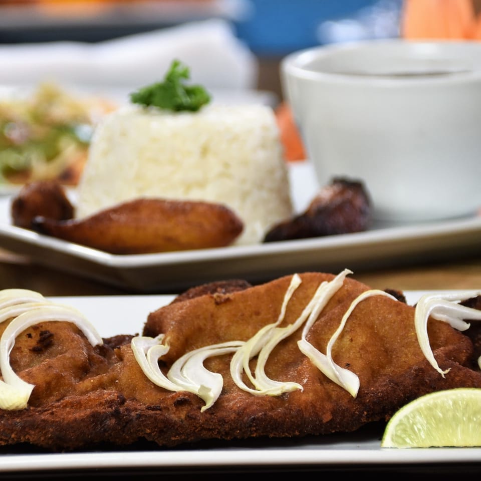 Crispy fried fish fillet garnished with shredded cabbage and lime, served with rice and vegetables.