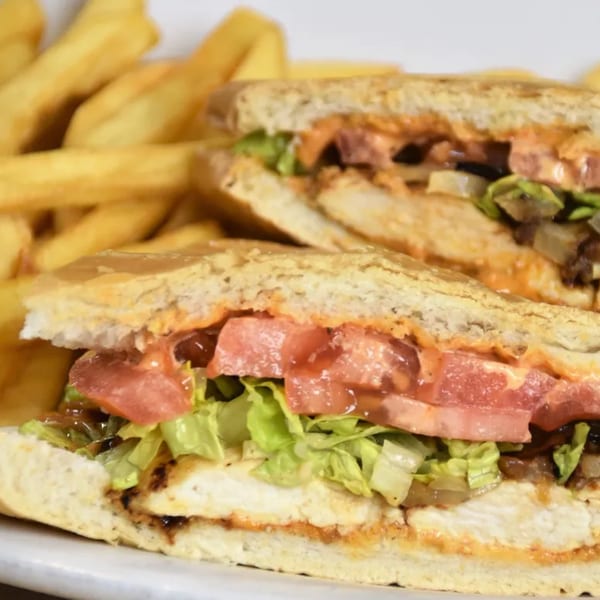 Cuban chicken sandwich with lettuce, tomato, and sauce, served with golden french fries.