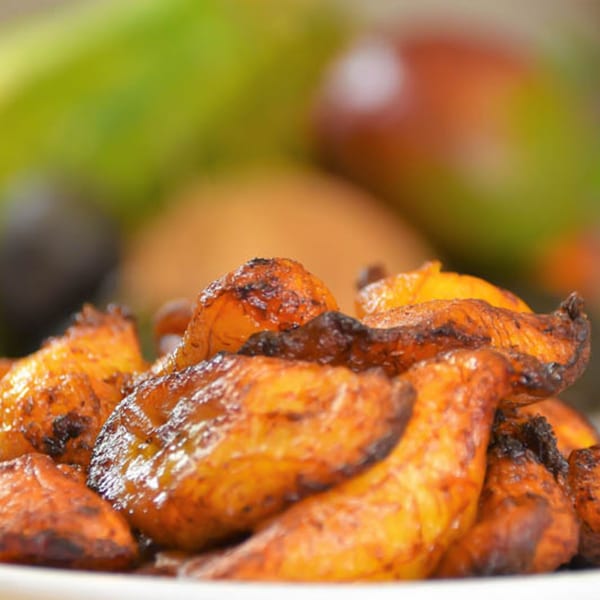 Close-up of golden-brown fried plantains, a Cuban delicacy, with a blurred green background.