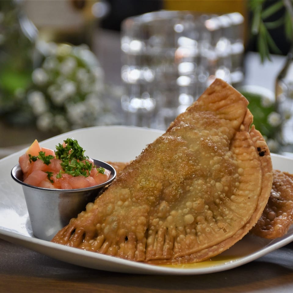 Golden fried fish-shaped pastry served with diced tomato salsa and herbs on a white plate.
